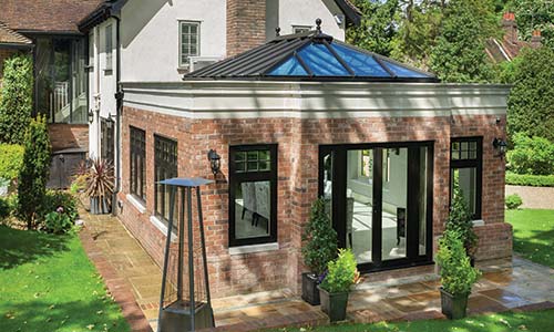 large conservatrory with residence windows and doors installed with patio and fire in garden title=